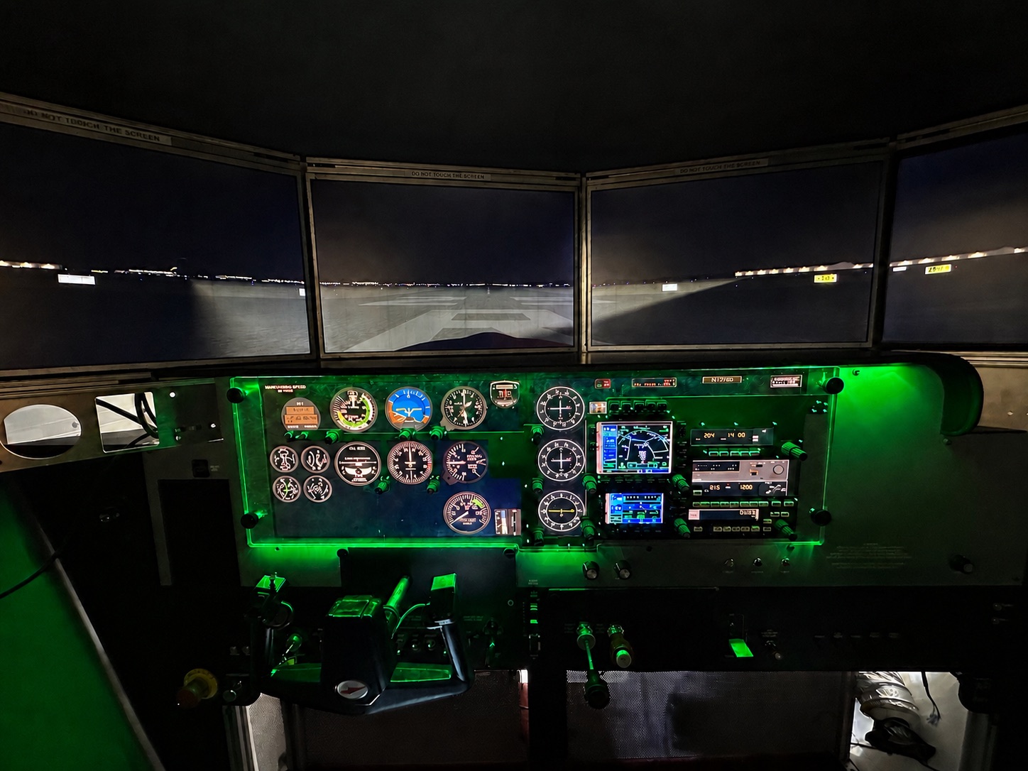 Home flight simulator cockpit with a lit instrument panel and multi-screen visual display